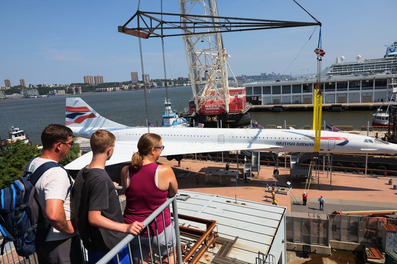 Three people watch as the British Airways Concorde, the fastest commercial aircraft in the world, is lifted away from the Intrepid Museum for renovations.