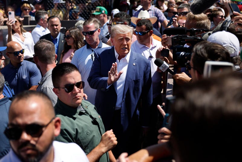 Surrounded by campaign staff and members of the U.S. Secret Service, Former U.S. President Donald Trump (C) waves to supporters as he visits the Iowa Pork Producers Tent at the Iowa State Fair on August 12, 2023 in Des Moines, Iowa. 