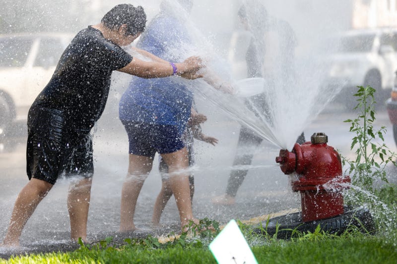 Kids and adults cool off beside an open fire hydrant