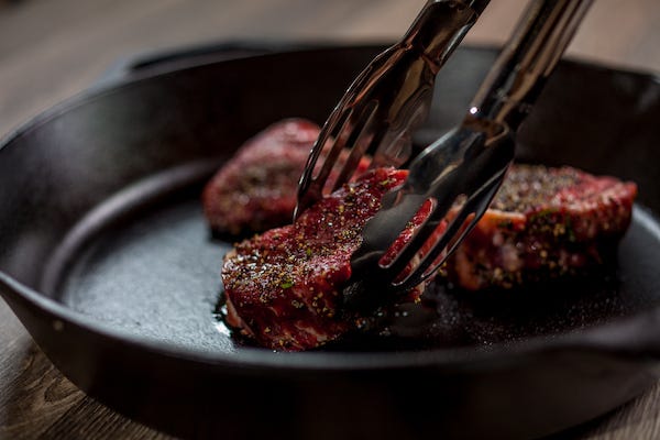 Placing steaks on a pan with tongs