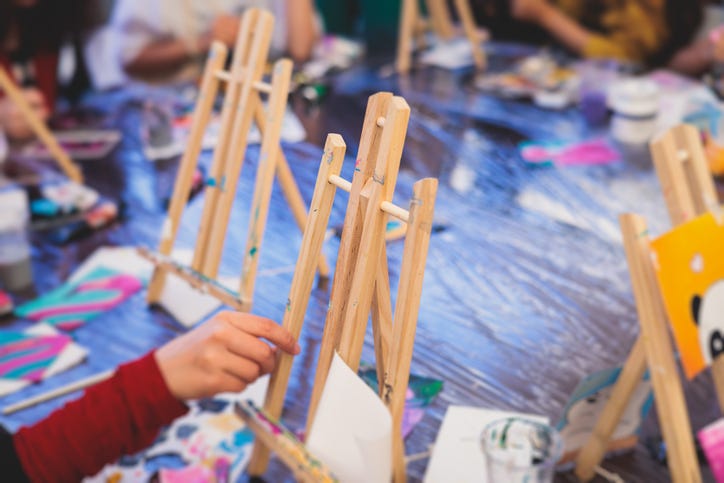 Process of painting, group class of young talented kids students with painting easels, and canvases during lesson of watercolour painting outdoors, drawing class for children in art school