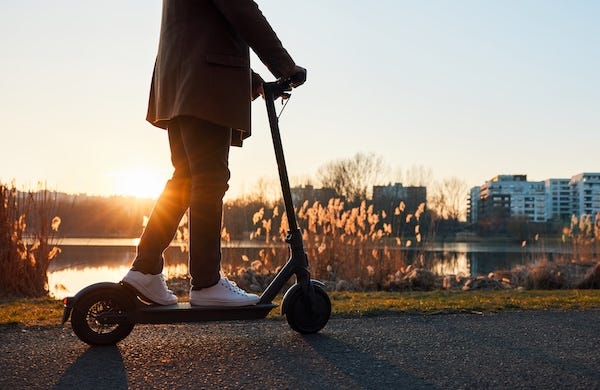 Man riding electric scooter in a park during sunset