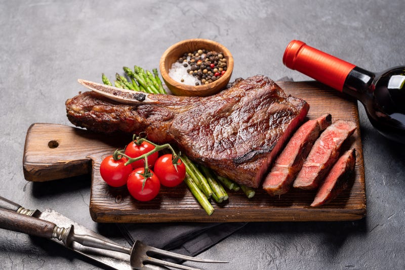 Medium rare grilled Tomahawk beef steak with asparagus and red wine