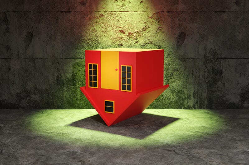 Red toy house upside down forming a down arrow on a concrete floor illuminated by a green spotlight. Illustration of the concept of falling house prices