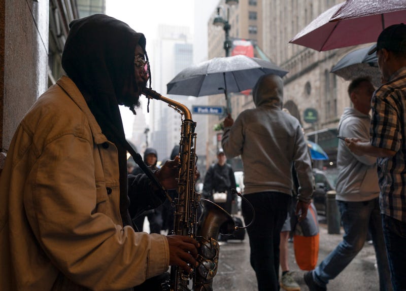A saxophonist plays in Manhattan as people walk by on Saturday. The weekend's rainy weather continues this week