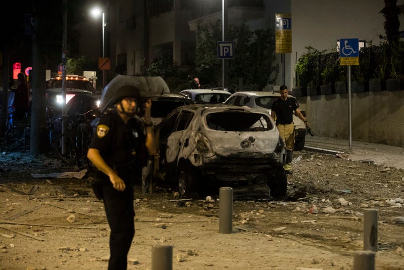 Police officer stand near a burned car at a scene where a rocket fired from Gaza strip hit a building on October 7, 2023 in Tel Aviv, Israel. 