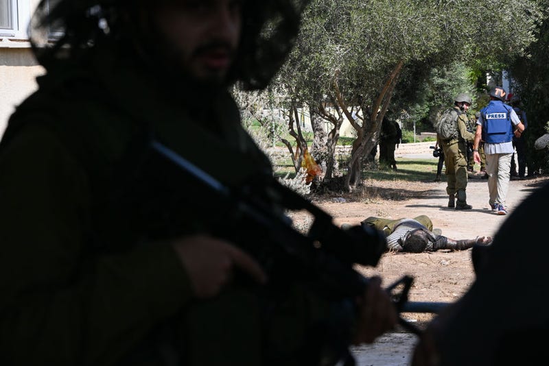 A member of the media and IDF soldiers walk past a Hamas militant who was killed days earlier after attacking this kibbutz where dozens of civilians were killed near the border with Gaza, on October 10, 2023 in Kfar Aza, Israel. Israel has sealed off Gaza and conducted airstrikes on Palestinian territory after an attack by Hamas killed hundreds and took more than 100 hostages. On October 7, the Palestinian militant group Hamas launched a surprise attack on Israel from Gaza by land, sea, and air, killing over 700 people and wounding more than 2000. Israeli soldiers and civilians have also been taken hostage by Hamas and moved into Gaza. The attack prompted a declaration of war by Israeli Prime Minister Benjamin Netanyahu, and ongoing retaliatory strikes by Israel on Gaza killing hundreds.(Photo by Alexi J. Rosenfeld/Getty Images)