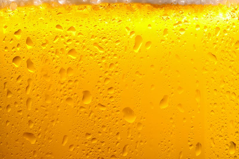 Glass of tasty cold beer with foam and condensation drops as background, closeup