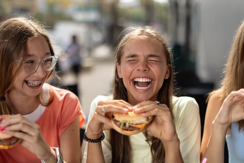 Laughing teenage girls eating hamburgers