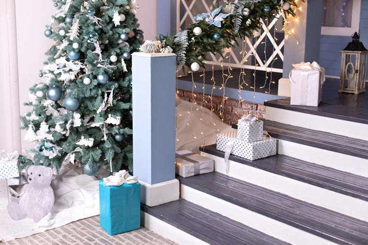 Festive outdoor design home with Xmas tree and gifts in yard. House entrance staircase decorated for winters holidays, gifts, branches fir and glowing garland. Cozy wooden porch of the house with gift