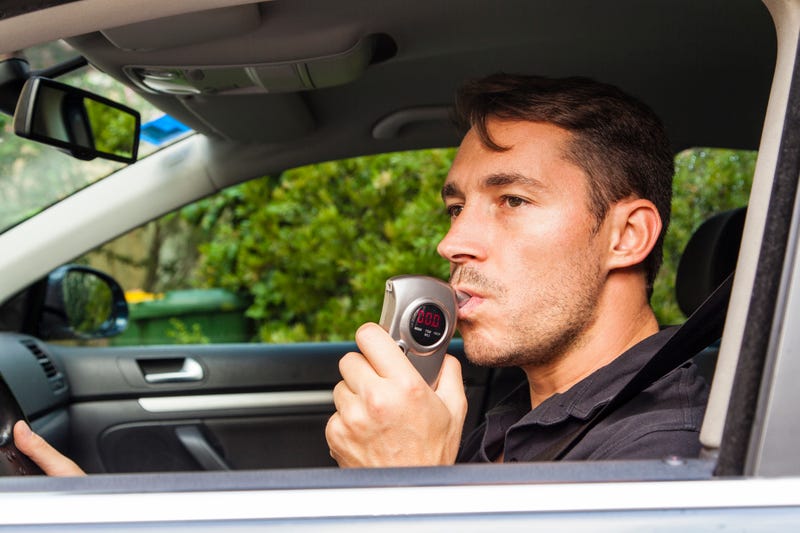 Man blowing into car breathalyzer. Stock photo.