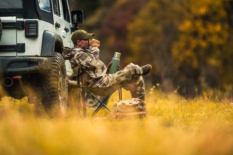 Hunter sitting next to his vehicle drinking coffee