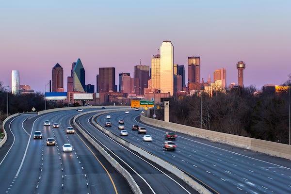 Cars driving against downtown Dallas skyline during the evening