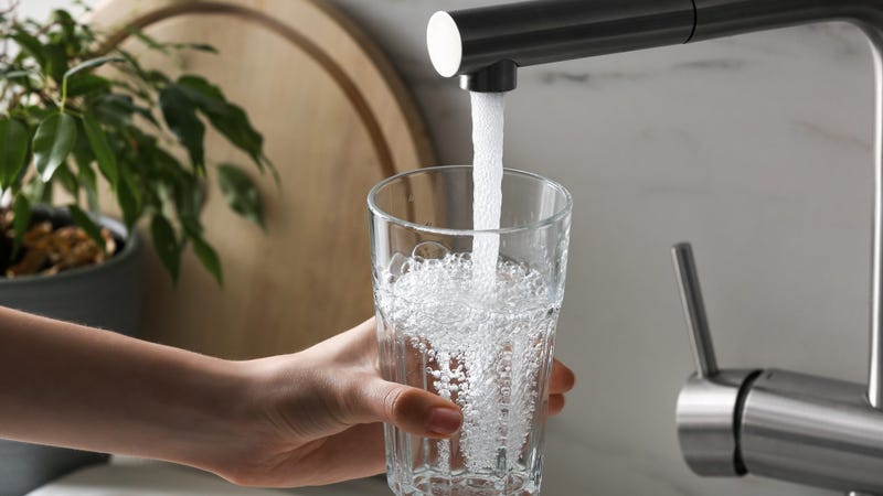 Woman filling glass with tap water from faucet in kitchen