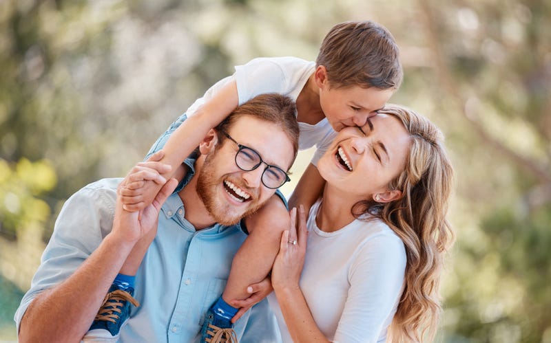 Happy, love and young boy kid kissing his mother on his father shoulders in an outdoor park or field.
