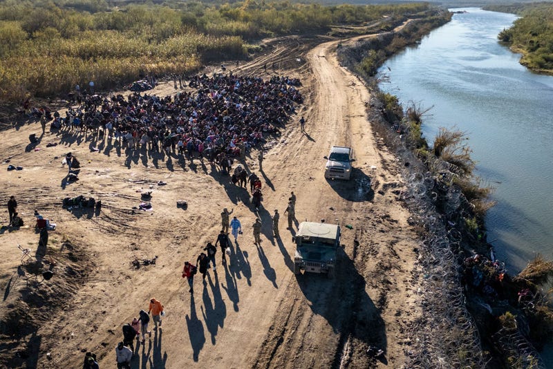 In this aerial view, Texas National Guard troops direct a group of more than 1,000 immigrants towards a U.S. Border Patrol processing center after they crossed the Rio Grande from Mexico on December 18, 2023 in Eagle Pass, Texas.