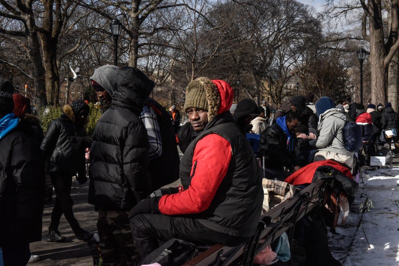 Homeless migrants look on as food and clothing donations are distributed in Tompkins Square Park on January 20, 2024