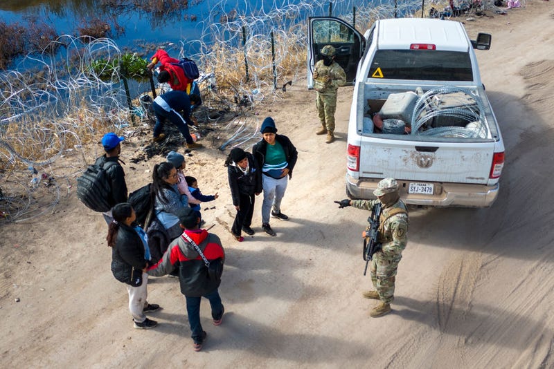 Seen from an aerial view, a Texas National Guard soldier speaks with immigrants after they passed through razor wire at the U.S.-Mexico border into El Paso, Texas on January 31, 2024 from El Paso, Texas. 