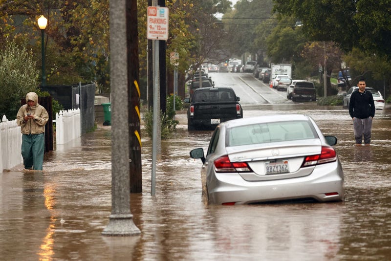 People gather along a flooded street as a powerful long-duration atmospheric river storm, the second in less than a week, impacts California on February 4, 2024 in Santa Barbara, California. The storm is delivering potential for widespread flooding, landslides and power outages while dropping heavy rain and snow across the region.