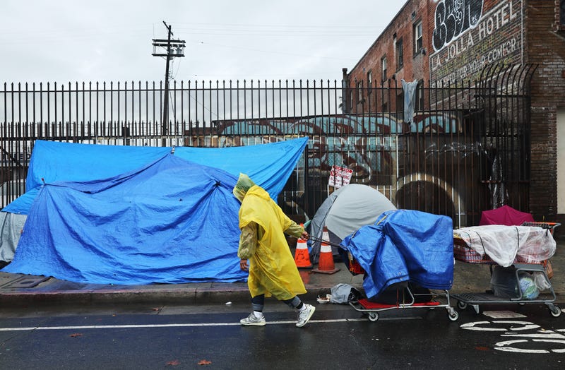 A person walks with carts in the rain near an encampment of unhoused people in Skid Row as a powerful long-duration atmospheric river storm, the second in less than a week, continues to impact Southern California on February 6, 2024 in Los Angeles, California. Over seven inches of rain have fallen in downtown Los Angeles during the storm, half the average yearly total. The storm delivered widespread flooding, landslides and power outages while dropping heavy rain and snow across the region. Skid Row is home to thousands of people who are either experiencing homelessness on the streets or living in shelters