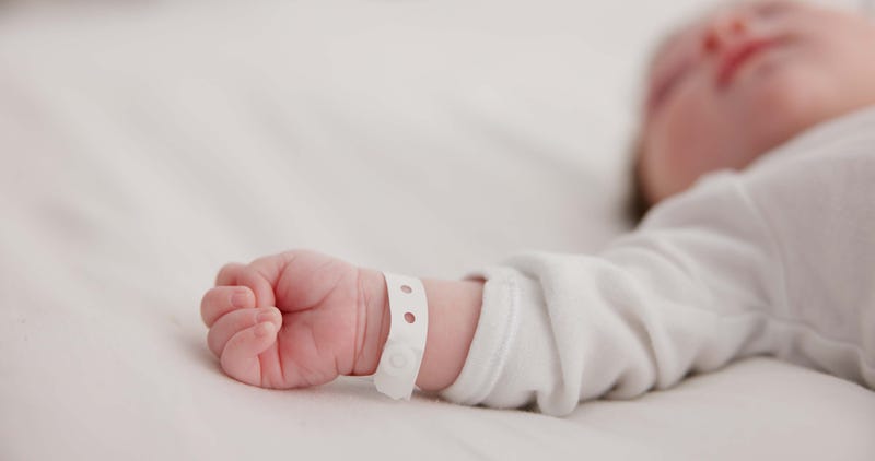 Baby, new born and hand with bracelet on bed for care