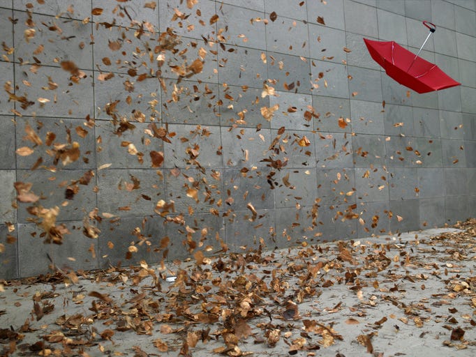 A wall mad of large gray polished stone. Leaves blow past in high winds. An umbrella flies through the air.