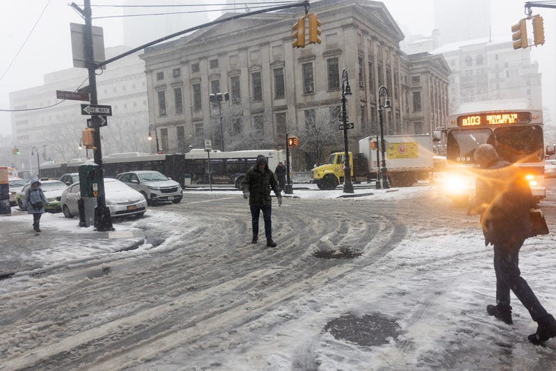 Vehicles and people navigate the snow in Downtown Brooklyn on February 13, 2024