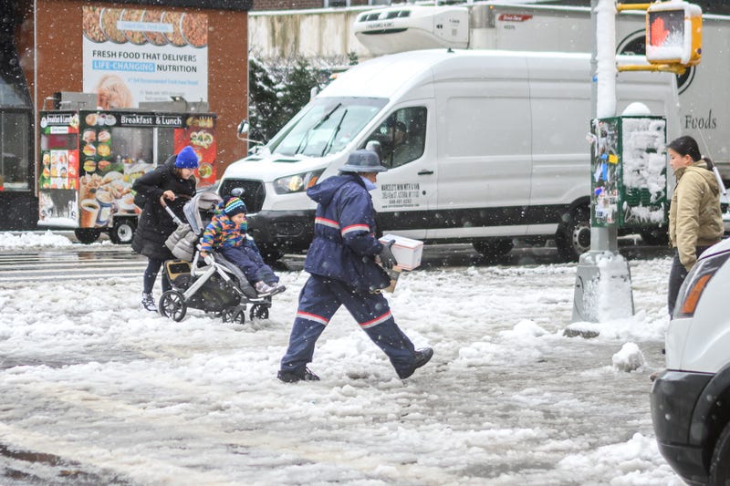 A USPS worker carrying a box and USPS flat rate box walks through the snow in Manhattan as a large winter storm makes its way across the area on February 13, 2024