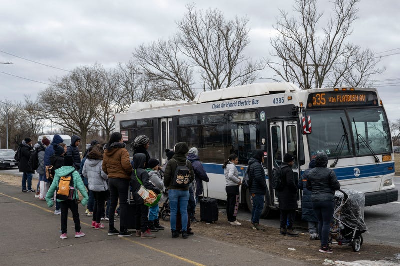 Recently arrived migrants wait at a bus stop outside Floyd Bennet Field shelter on February 21, 2024 in Brooklyn