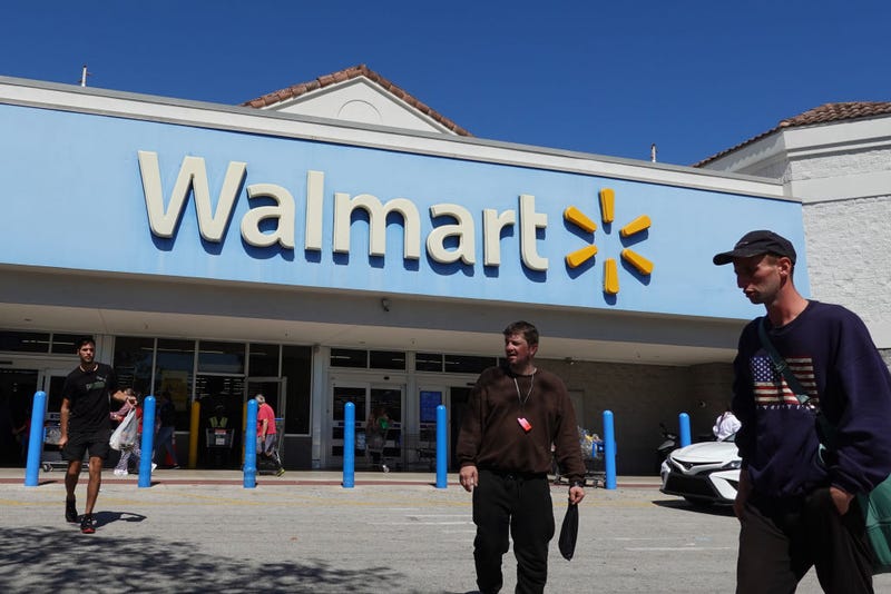 : People walk near the entrance to a Walmart Supercenter 