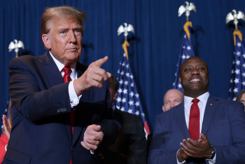 Republican presidential candidate and former President Donald Trump gestures to supporters as Sen. Tim Scott (R-SC) looks on during an election night watch party at the State Fairgrounds on February 24, 2024 in Columbia, South Carolina. Trump defeated Republican presidential candidate, former U.N. Ambassador Nikki Haley in her home state as South Carolina held its primary today.