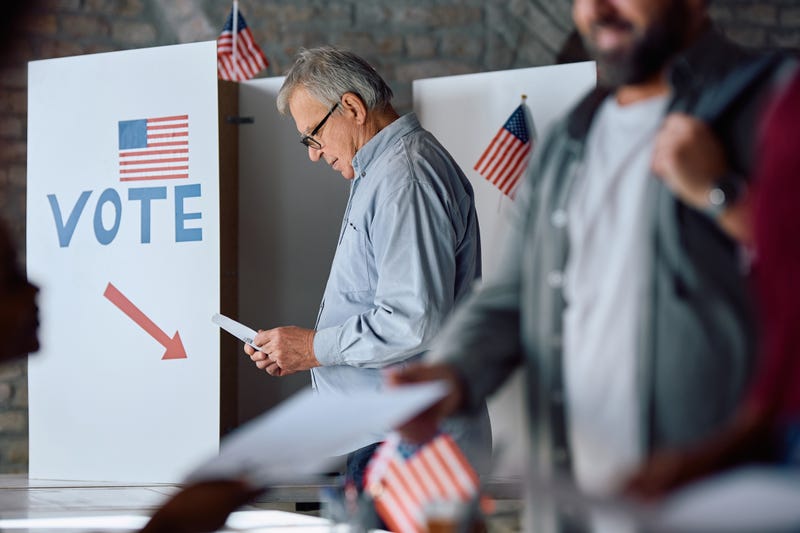 Senior man with a ballot at voting booth during US elections.
