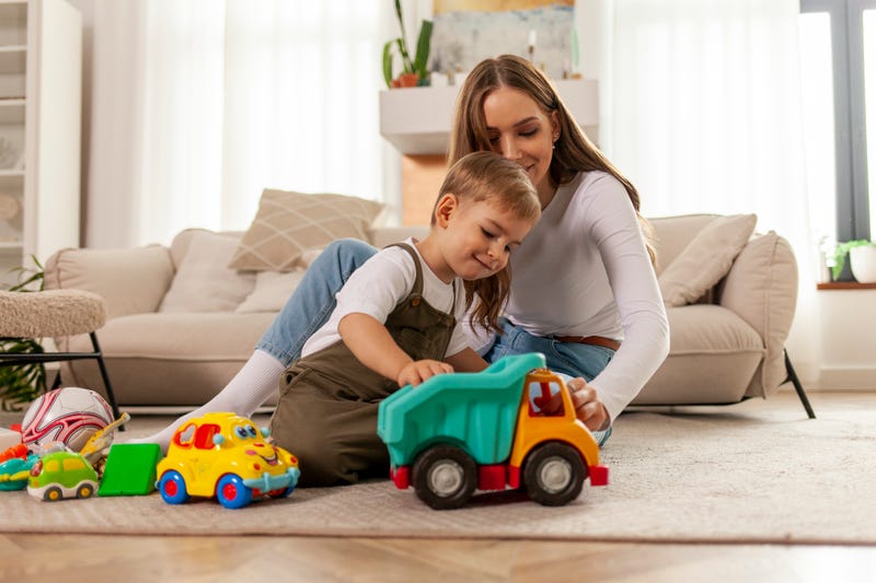 young mother plays with her little son with toys at home and smiles, 2-year-old boy plays with toy car with his parent, woman has fun with her child
