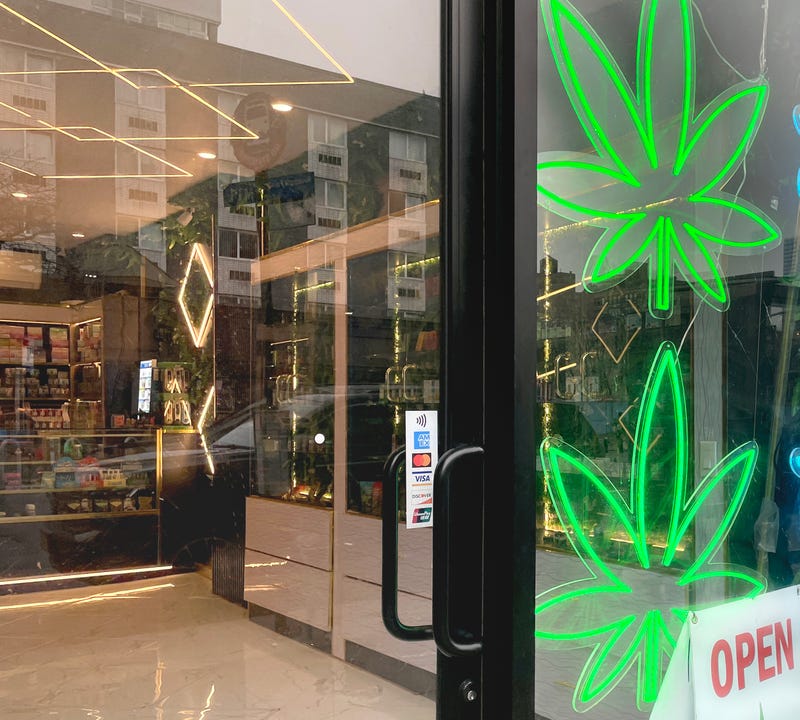 A green neon cannabis Leaf and an open sign in the window of an unlicensed smoke shop selling cannabis in New York City