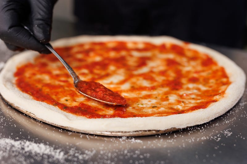 A cook spreads sauce on a pizza crust.