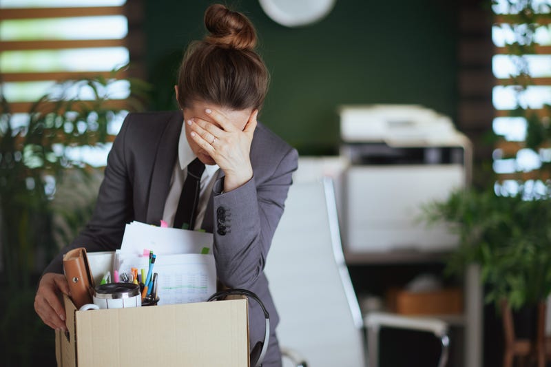 New job. unhappy modern female employee in modern green office in grey business suit with personal belongings in cardboard box.