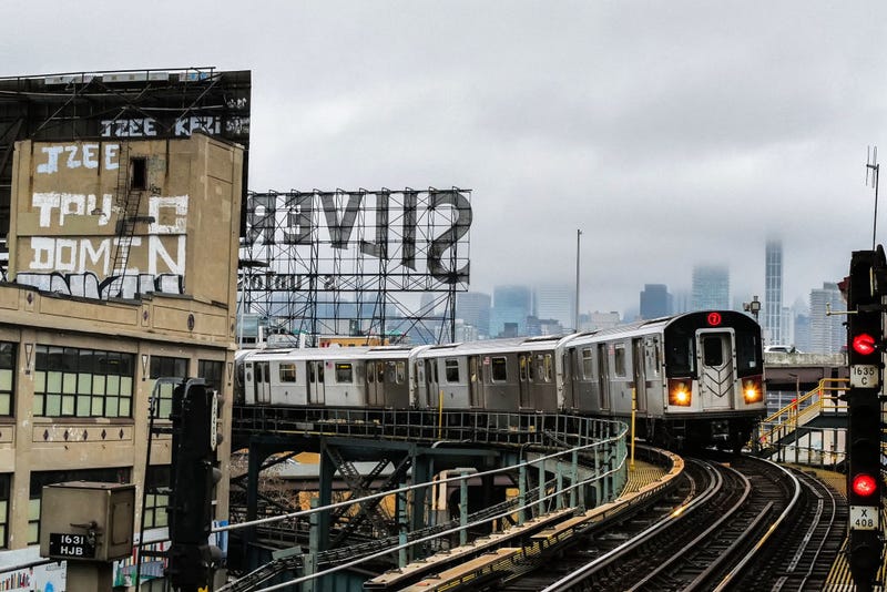 A "7" line train arrives at Queensboro plaza station in Queens, New York, as the Manhattan midtown skyline looms in the distance, on April 11, 2024.