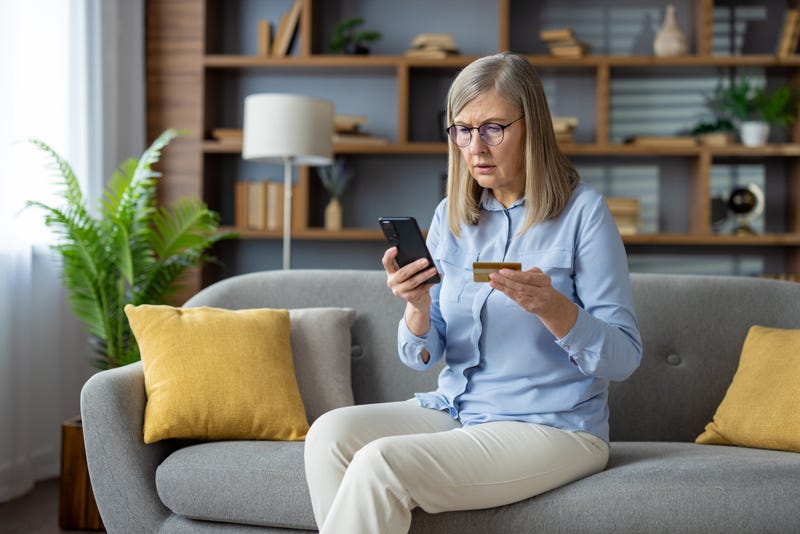 Confused older woman holds credit card in one hand and phone in other
