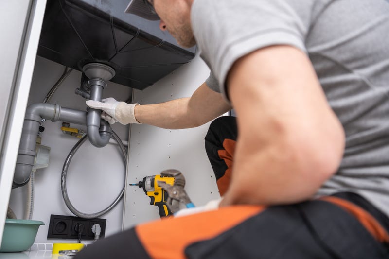 A plumber works on a drain pipe.