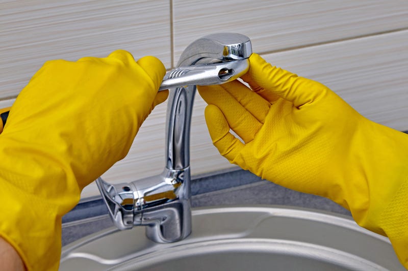 Kitchen faucet repair. A worker in yellow rubber gloves uses an adjustable wrench to unscrew the aerator.