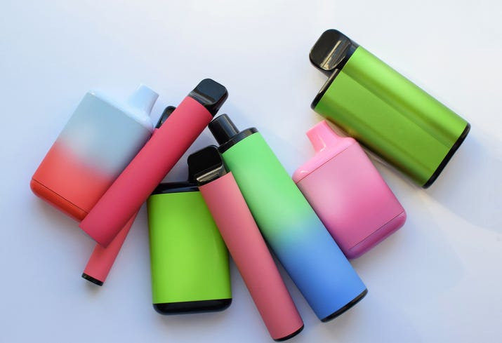Several multi-colored electronic cigarettes lie on a light table.