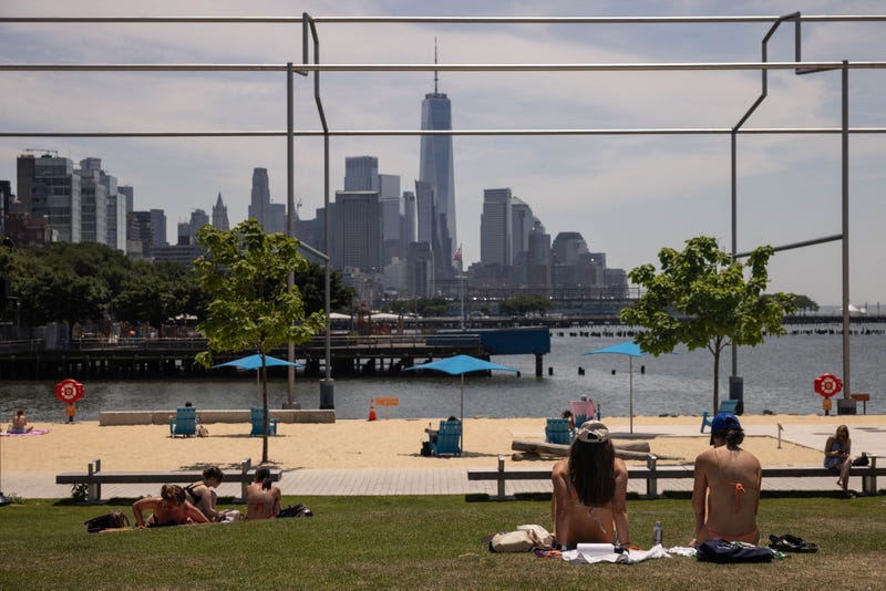 People sit in the grass along the Hudson River during a heatwave on June 20, 2024