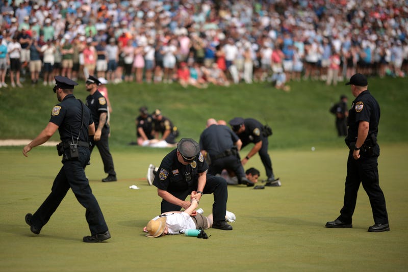 Climate change protestors are ushered off the 18th green by police officers during the final round of the Travelers Championship at TPC River Highlands on June 23, 2024 in Cromwell.