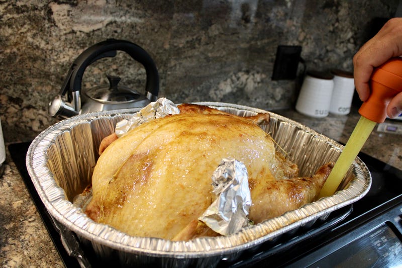 A man using a baster to baste a turkey with the juice from the bottom of the pan