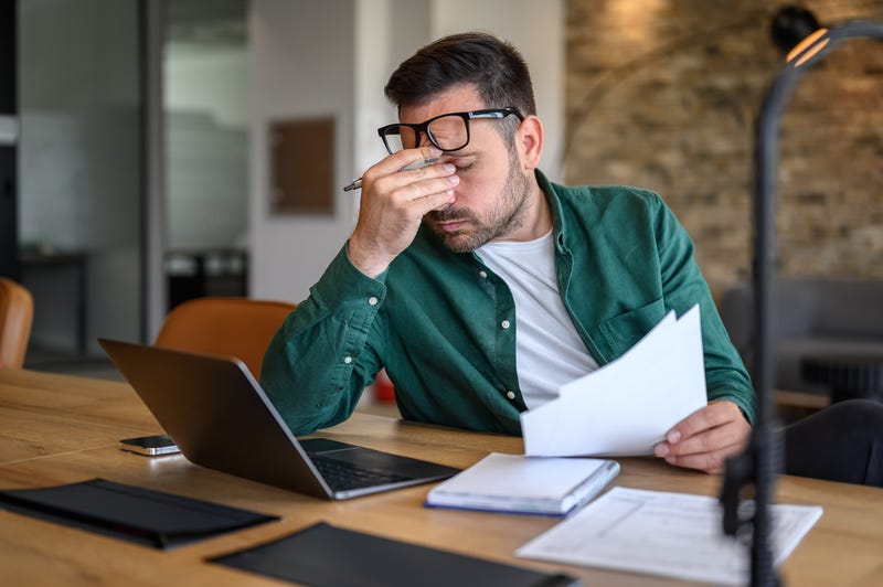Anxious male financial advisor rubbing eyes while working over laptop and analyzing reports at desk.