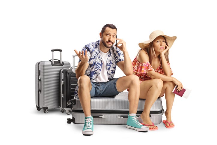 Young couple sitting on a suitcase and using a smartphone isolated on white background
