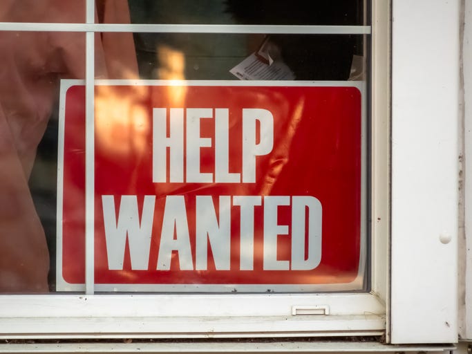 A red HELP WANTED sign displayed prominently in a store window, signaling the business's need for additional staff.