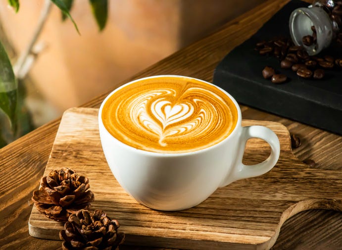 Heart Shaped Latte Art in a White cup with coffee beans isolated on wooden table