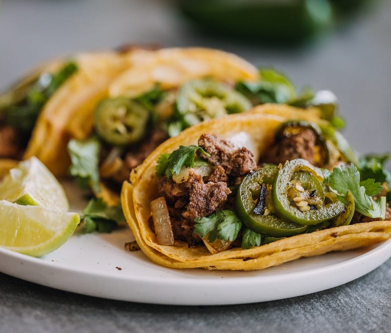 Tacos on a plate with fresh jalapeño, onion and cilantro