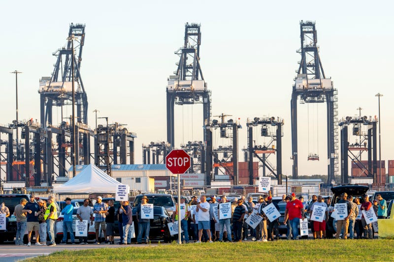 Shipping container cranes are visible in the background as Longshoremen carry signs and chant 